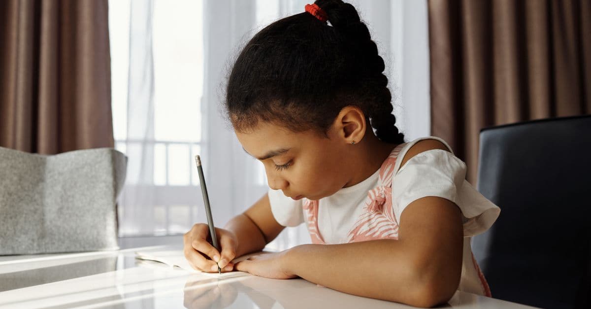 A focused young girl writing at her desk, absorbed in her homework task at home.