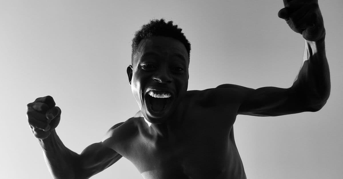 Energetic monochrome portrait of a shirtless man celebrating with fists raised.
