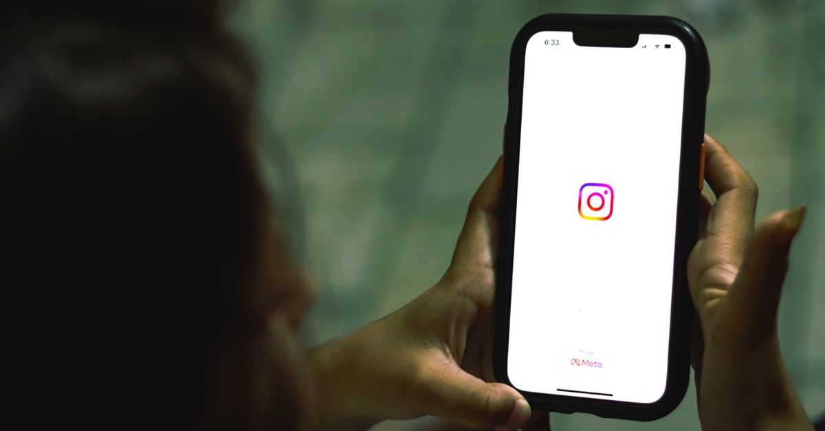 Close-up of a woman holding a smartphone displaying the Instagram app indoors.